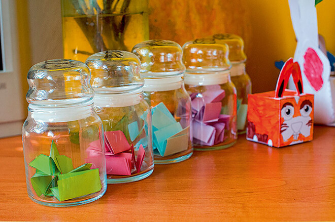 Uz galda piecas mazas burciņas ar glīti salocītām papīra lapiņām – sakrātiem labajiem darbiem.