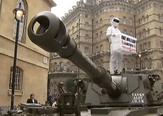 "Gāzi grīdā" Stiga apģērbā ietērpta persona uz tanka, rokās tur plakātu "Atjaunot Klārksonu".
