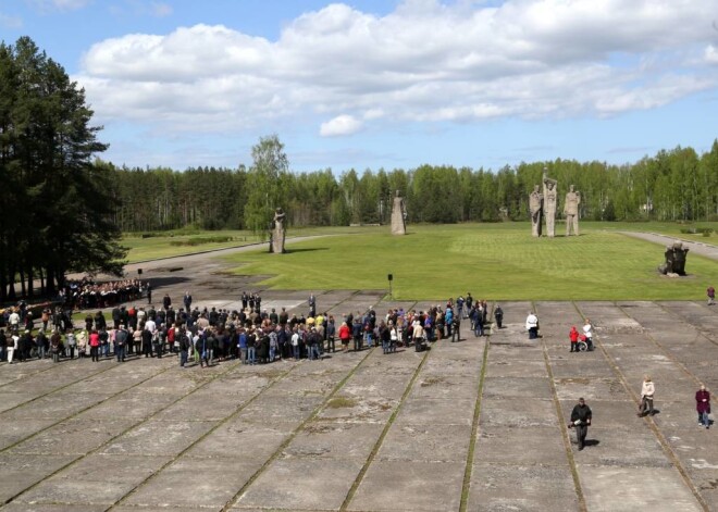 Cilvēki, tostarp amatpersonas, ar ziediem piedalās piemiņas brīdī Salaspils memoriālā, kas veltīts nacisma sagrāvei un Otrā pasaules kara upuru piemiņai.