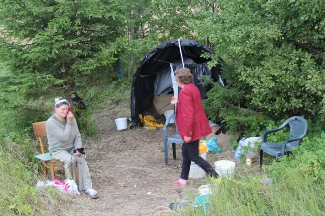 Sieviete ik dienu pavada šosejas malā, dzīvojoties pie uzslietas plēves nojumes. Tur viņas gan pusdieno, gan ada zeķes, gan tirgo pašu lasītās meža veltes.