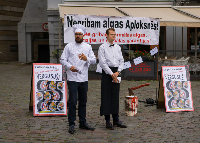 Vecrīgā aktīvisti ar plakātiem un cirvi protestē pret aplokšņu algām