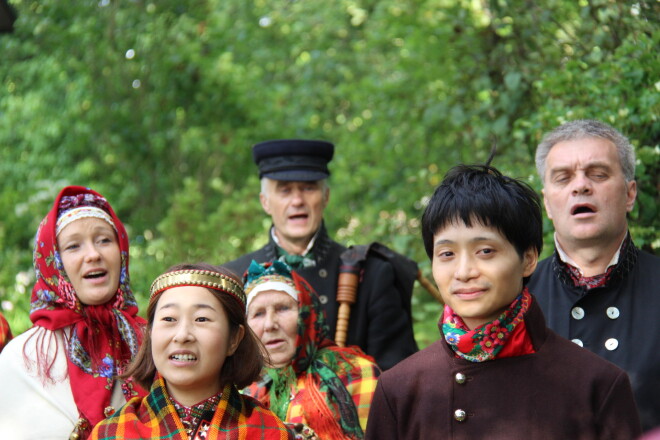 Gobu māju dārzā notiek mičošana suitu tradīcijās. Norie un vīrs Rjūša Kozaki, vedēji Māra un Grigorijs Rozentāli, Norie Latvijas vecāmiņa Ručs un Suitu dūdenieku vadītājs Juris Lipsnis.