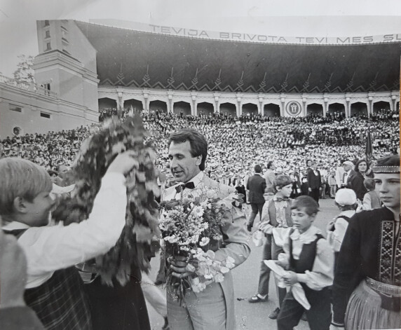 Puķes diriģentam. V Skolu jaunatnes dziesmu un deju svētkos Mežaparka estrādē 1984. gadā.