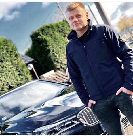 Pāvels Rebenoks pozē pie spožas BMW automašīnas.