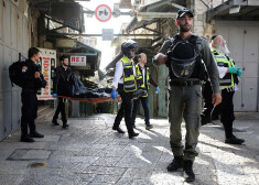 Izraēlas policists sargā uzbrukuma apkārtni, kamēr mediķi aiznes nošautā palestīnieša mirstīgās atliekas.