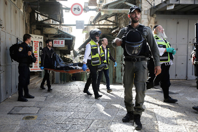 Izraēlas policists sargā uzbrukuma apkārtni, kamēr mediķi aiznes nošautā palestīnieša mirstīgās atliekas.