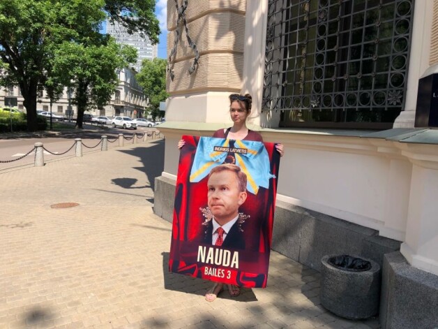 Tikmēr pie Latvijas bankas durvīm par tās prezidenta lēmumu pēc ilga laika parādīties tribīnē protestēja vairāki ļaudis. Kāda vecāka kundze ar šādu plakātu bija pamanījusies iekļūt preses konferences telpā un nostājās blakus Rimšēvičam.