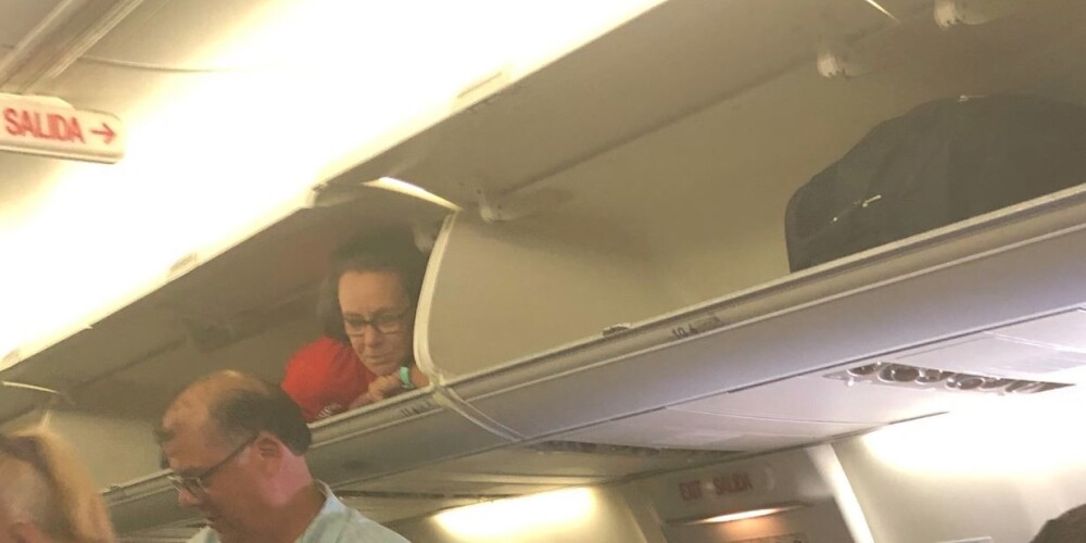 FOTO: lidmašīnas stjuarte sagaida pasažierus, paslēpusies rokas bagāžas nodalījumā