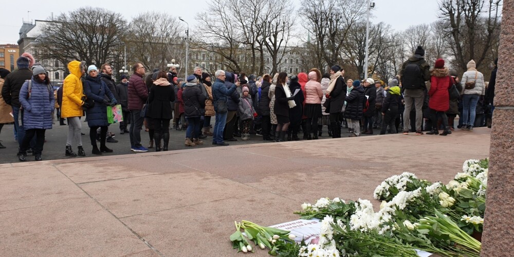 Cilvēku pūlis pie Brīvības pieminekļa ar baltiem ziediem pauž atbalstu Kristīnei Misānei