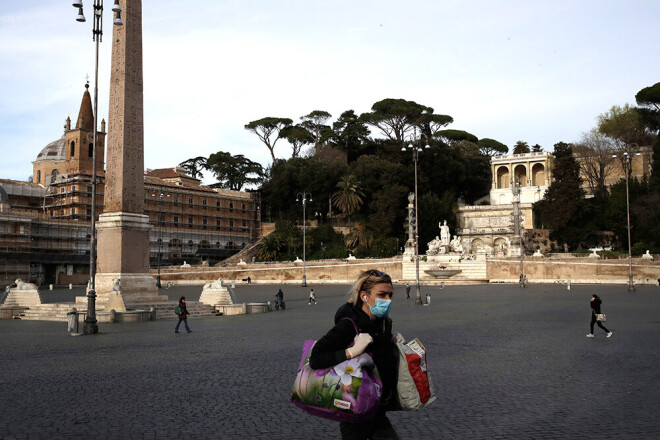 Sieviete ar sejas masku Romā šķērso Piazza del Popolo laukumu.