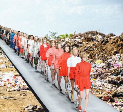 Jaunu tērpu modes skate atkritumos izmestu apģērbu kalnu ielenkumā.