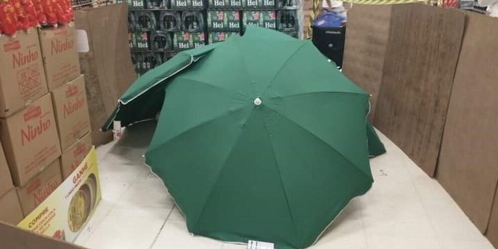 Sašutums Brazīlijā: cilvēki iepērkas blakus mirušam darbiniekam, kurš paslēpts zem lietussargiem