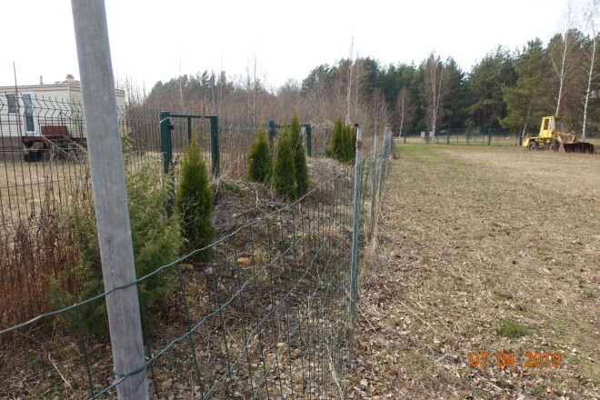 Reinholdu uzliktajam zaļajam žogam priekšā Juris Ozoliņš uzlicis otru žogu (pelēkā krāsā), bez vārtiņiem. Lai vēl vairāk apgrūtinātu piekļuvi pie īpašuma, izbēris būvgružu kaudzes.