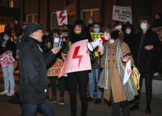 Pretrunīgi vērtētā nodibinājuma "Tautas varas fronte" pārstāvis Roberts Raimo pietuvojas jaunatnes organizācijas "Protests" pārstāvēm, kuras pauž neapmierinātību, ka vīrietis neievēro distanci un ir bez maskas.