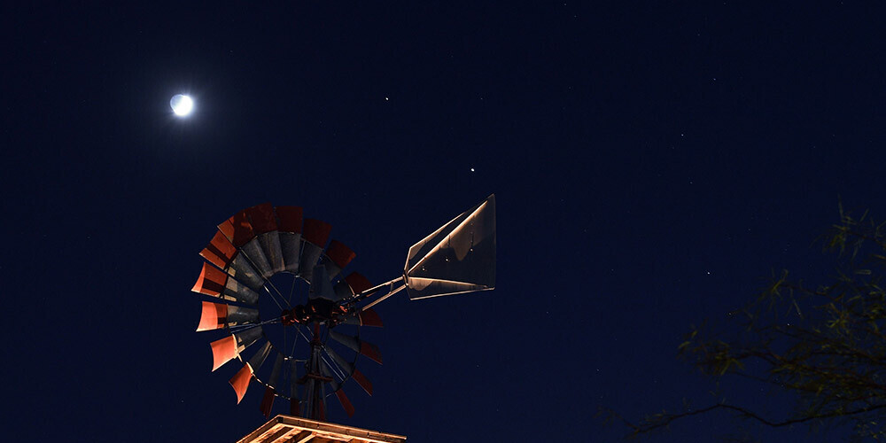Mēness un planētas Saturns un Jupiters, kas redzamas virs vējdzirnavām Nevadā.