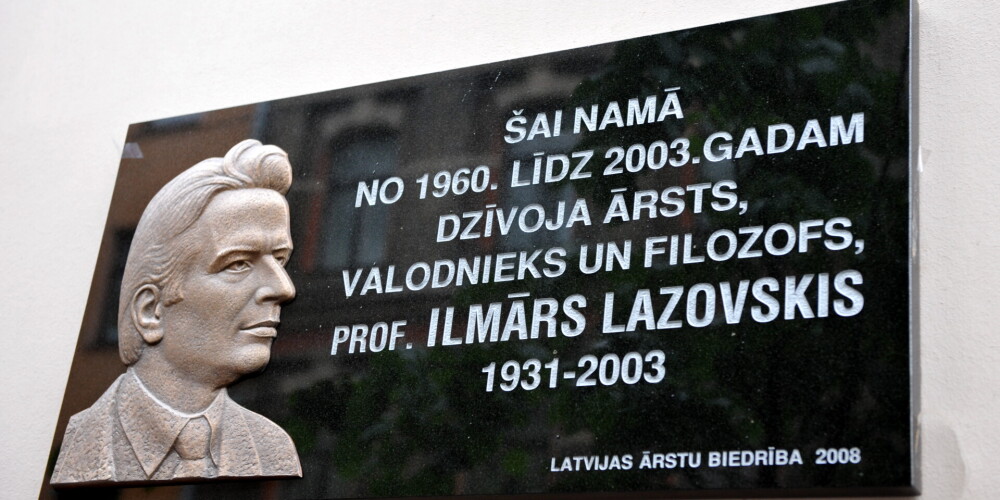 Plāksne ar cilni un uzrakstu "Šai namā no 1960.gada līdz 2003.gadam dzīvoja ārsts, valodnieks un filozofs, profesors Ilmārs Lazovskis (1931-2003)" pie nama Rīgā, Martas ielā 9.