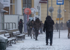 Cilvēki sabiedriskā transporta pieturvietā sniegputeņa un vētras laikā.