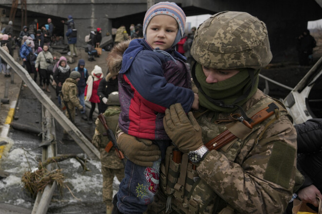 Ukrainas karavīrs palīdz bērnam tikt pāri upei Irpinā. Tiltu pār upi sabombardējuši Krievijas gaisa spēki. 2022. gada 5. marts. 