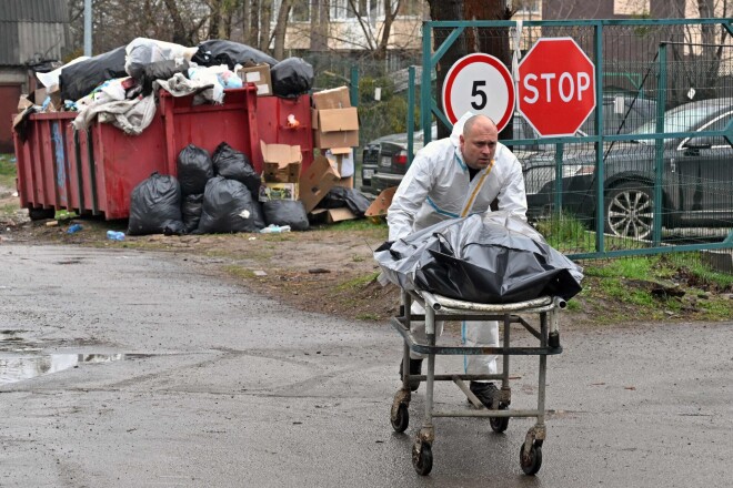 Vīrietis nogādā maisus ar civiliedzīvotāju līķiem uz automašīnu. Buča,  2022. gada 22. aprīlis.
