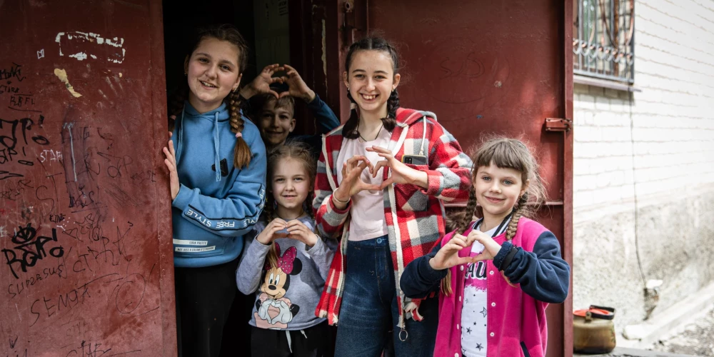 2022. gada 26. maijs, Lisičanska, Ukraina: bērni, kas dzīvo pazemes bumbu patvertnē, rāda sirds simbolu ārpus savas patvertnes.