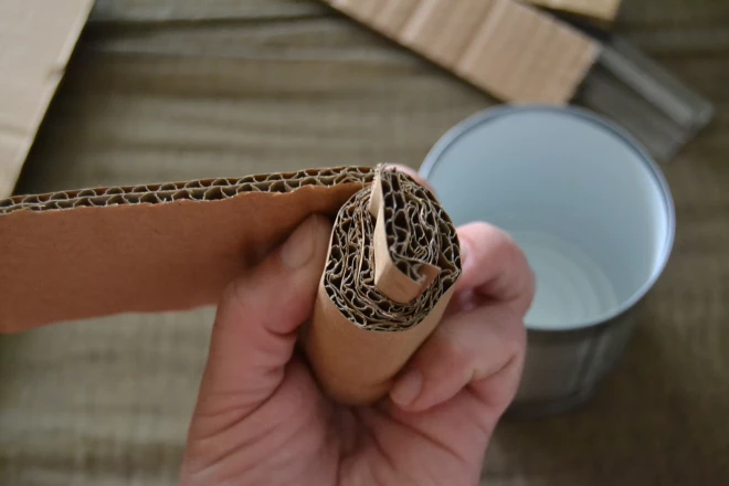 Iepakojuma kartonu ar biezo gofrējumu sagriež loksnēs un sarullē atbilstīgi bundžas izmēram.