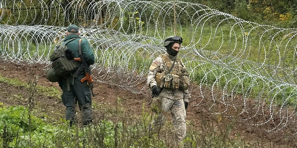 Latvijas robežsargs ar karavīru pie pagaidu dzeloņstiepļu žoga uz robežas ar Baltkrieviju netālu no Robežniekiem.