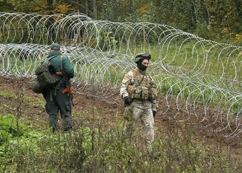 Latvijas robežsargs ar karavīru pie pagaidu dzeloņstiepļu žoga uz robežas ar Baltkrieviju netālu no Robežniekiem.