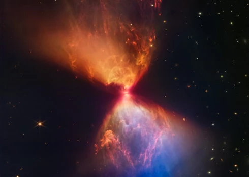 šajā izdales materiāla attēlā, ko 2022. gada 16. novembrī izdeva NASA, izmantojot NASA/ESA/CSA Džeimsa Veba kosmosa teleskopa tuvās infrasarkanās kameras (NIRCam) instrumentu, ir redzama protozvaigzne tumšajā mākonī L1527, kas ir iestrādāta materiāla mākonī, kas baro tā augšanu. - Džeimsa Veba kosmiskais teleskops trešdien atklāja savu jaunāko debesu varenības attēlu, ēterisku oranžu un zilu putekļu smilšu pulksteni, kas tika izšauts no jaunizveidojušās zvaigznes tā centrā. 