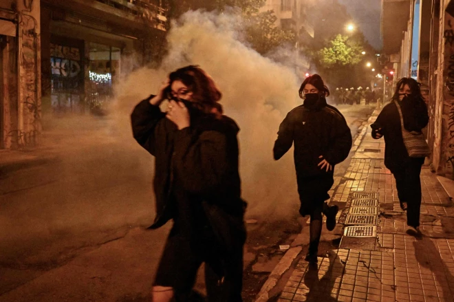 Women run away from tear gas smoke during clashes on the sidelines of a rally against police violence, marking the 14th anniversary of the 2008 fatal police shooting of a teenager in central Athens's Exarchia neighbourhood on December 6, 2022. - Thousands of protesters demonstrated in Athens, Thessaloniki and other Greek cities against police violence, a day after a Roma youth was shot in the head in a police pursuit. The demonstrations were part of planned annual commemorations to mark the 2008 death of Alexandros Grigoropoulos, a 15-year-old fatally shot by police. (Photo by Louisa GOULIAMAKI / AFP)