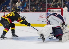 "Canucks" uzbrucējs  Andrejs Kuzmenko vēro, kā  Elīass Petešona mestā ripa izslīdz caur "Blue Jackets" vārstsarga Jonasa Korpisalo kājām.