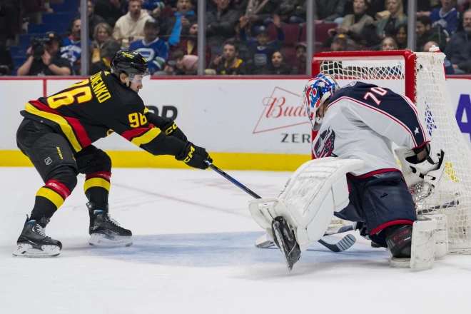 "Canucks" uzbrucējs  Andrejs Kuzmenko vēro, kā  Elīass Petešona mestā ripa izslīdz caur "Blue Jackets" vārstsarga Jonasa Korpisalo kājām.