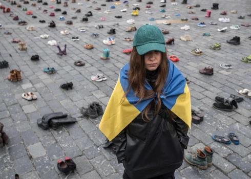 Ukrainas karogā ietērpusies ukraiņu dizainere Margarita Čala stāv līdzās kurpēm, kas simbolizē kara noziegumus, kas pastrādāti pret ukraiņu civiliedzīvotājiem vecpilsētas laukumā Prāgā, Čehijā, lai atzīmētu viena gada jubileju kopš Krievijas iebrukuma Ukrainā 2023. gada 15. janvārī.