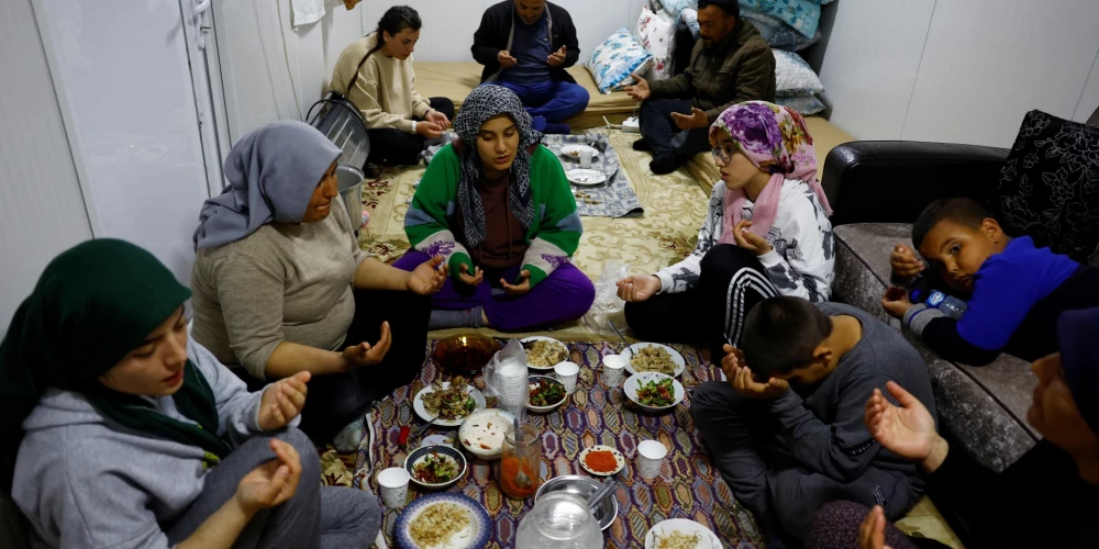 Members of the Arslan family pray at dinner in one of the three container homes where they live by a petrol station after losing their homes in the aftermath of a deadly earthquake in Nurdagi, Turkey, March 4, 2023. REUTERS/Susana Vera
