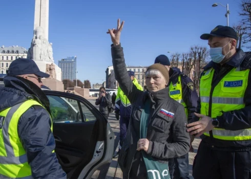 Valsts policijas darbinieki leģionāru gājiena laikā pie Brīvības pieminekļa aiztur sievieti, kuras apģērbu rotā pie krūtīm piešūts Krievijas karodziņš (Foto: LETA)