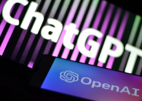 Fotoattēla ilustrācija ar "ChatGPT" un "OpenAI" pētniecības laboratorijas logotipu un uzrakstu mobilā tālruņa viedtālruņa ekrānā ar izplūdušu fonu. 