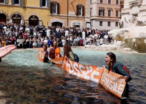 Klimata aktīvisti tur plakātu kokogļu ielēšanas Trevi strūklakas ūdenī demonstrācijas laikā pret fosilo kurināmo Romā, Itālijā, 2023. gada 21. maijā.