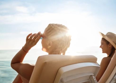 Young beautiful girls in swimwear sunbathing, lying on chaises near sea. Copy space.