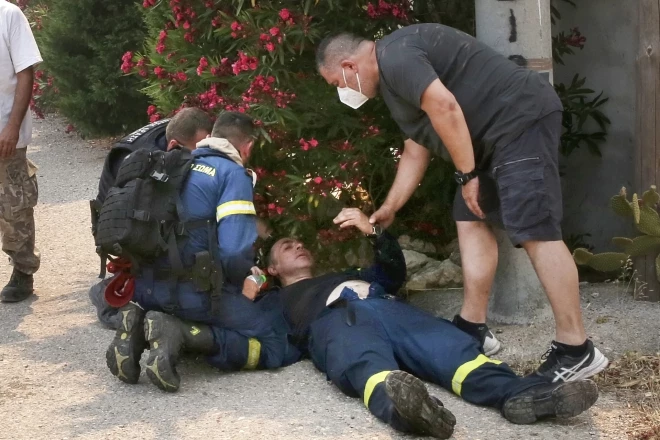 Пожарные оказывают первую помощь своему коллеге, получившему тепловой удар во время тушения пожара в районе Кандили Мегара в западной Аттике, Греция, 19 июля 2023 года.