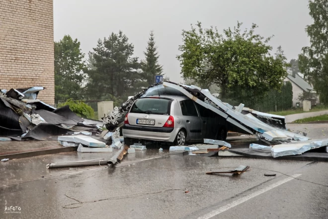 Pašvaldības visā Latvijā pašlaik aprēķina pirmdienas vētras nodarītos zaudējumus. Attēlā: ēkai norauta jumta saplacināta automašīna Madonā.