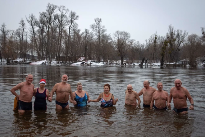 Cilvēki pozē fotogrāfijai Dņepras upes ledainajā ūdenī tradicionālo Epifānijas svētku laikā Kijivā.