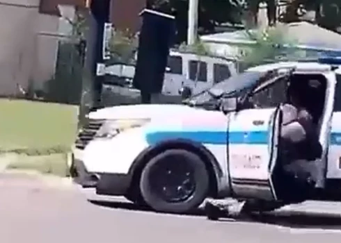 Templa mēģina aizdzīt policijas automašīnu, kamēr policists ieķēries durvīs (ekrānuzņēmums no video)