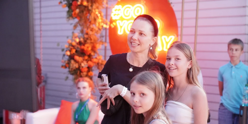 Madara Gobziņa ar meitām Marutu Agapi un Annu Mariju vēro TV ekrānā mūziķu uzstāšanos uz Dzintaru koncertzāles skatuves Laimas Vaikules festivālā. 