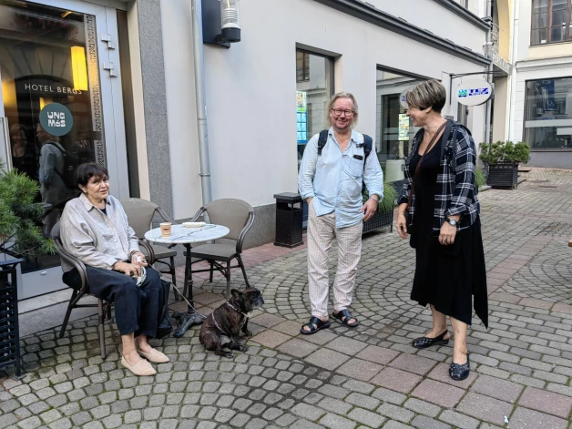 Velta Puriņa bija piesēdusi āra kafejnīcā ar suni Čeisu, kad viens aiz otra garāmejot pie viņas draudzīgi parunāt piestāja gan diriģents Ivars Cinkuss, gan muzikoloģe un žurnāliste Daiga Mazvērsīte.