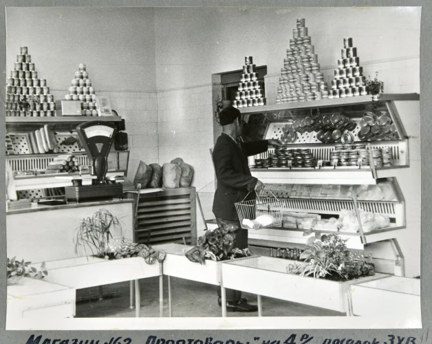 1969. gads, pārtikas veikals Daugavpilī. Izskatās, ka produktu ir daudz, taču, ja paskatīsimies uzmanīgāk, tad redzēsim, ka ir tikai dažas konservu šķirnes (lai izskatītos bagātīgāk, vitrīnā iebūvēts spogulis), kaut kas no piena produktiem, bet aiz letes vismaz ir arī, kā izskatās, pāris luņķi desas. 