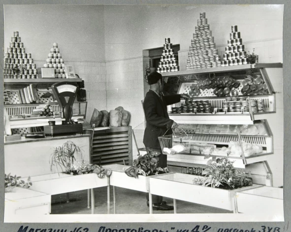 1969. gads, pārtikas veikals Daugavpilī. Izskatās, ka produktu ir daudz, taču, ja paskatīsimies uzmanīgāk, tad redzēsim, ka ir tikai dažas konservu šķirnes (lai izskatītos bagātīgāk, vitrīnā iebūvēts spogulis), kaut kas no piena produktiem, bet aiz letes vismaz ir arī, kā izskatās, pāris luņķi desas.
