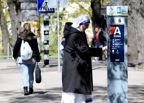 Sieviete pie autostāvvietas apmaksas automāta.