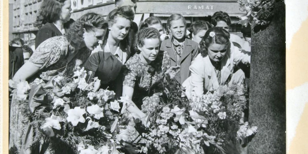 Padomju pilsoņi noliek ziedus pie Ļeņina pieminekļa. Fonā – grāmatnīca, no kuras logiem noraugās vai viss politbirojs. Piecdesmito gadu vidus.