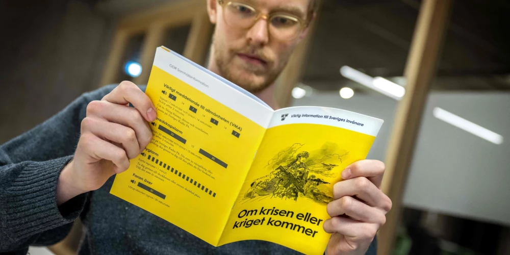 Vīrietis lasa informatīvo bukletu par to, kā rīkoties krīzes vai kara gadījumā