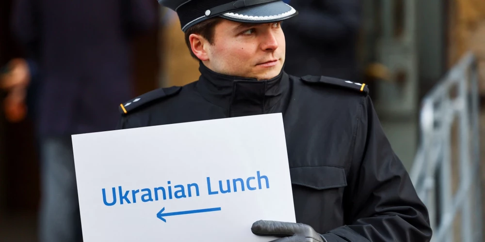 Vācijas armijas Bundesvēra biedrs Minhenes drošības konferencē Minhenē, Vācijā, 2025. gada 15. februārī, tur zīmi, kas informē par pusdienām ar Ukrainas prezidentu.