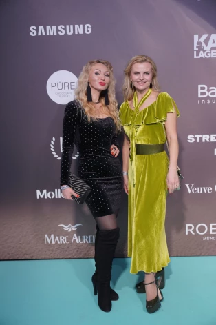Ilze Šipkēvica (pa labi) ar radinieci Ievu Baumgarti no sirds izbaudīja darba nedēļas noslēgumā notiekošā modes šova aktivitātes. Abas smaidīgas, jautrā noskaņojumā un skaisti saposušās, pozēja pie foto sienas.